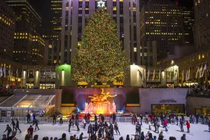 The Rockefeller Center Christmas tree is lit at night with ice skaters skating in front of it