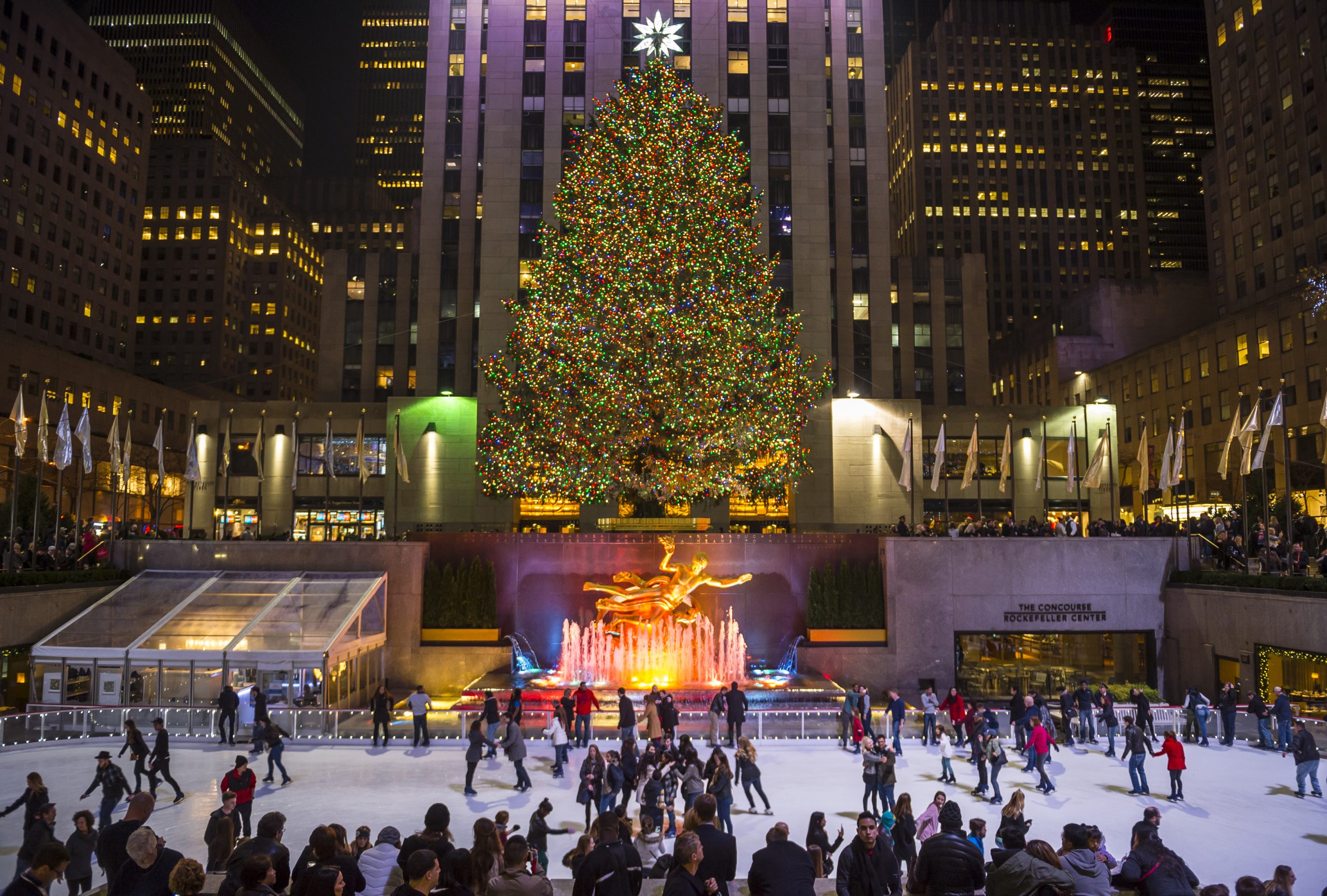 The Rockefeller Center Christmas tree is lit at night with ice skaters skating in front of it