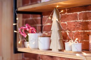 A shelf attached to a brick wall with Christmas decorations such as a wooden tree and a cup full of candy canes, and lights