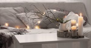 A white table and white couch are decorated with Christmas candles, twigs and lights