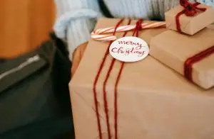 A woman holds a gift wrapped in brown paper and twine with a Merry Christmas tag