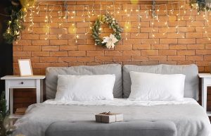 Christmas fairy lights on a wall behind a bed with a Christmas wreath