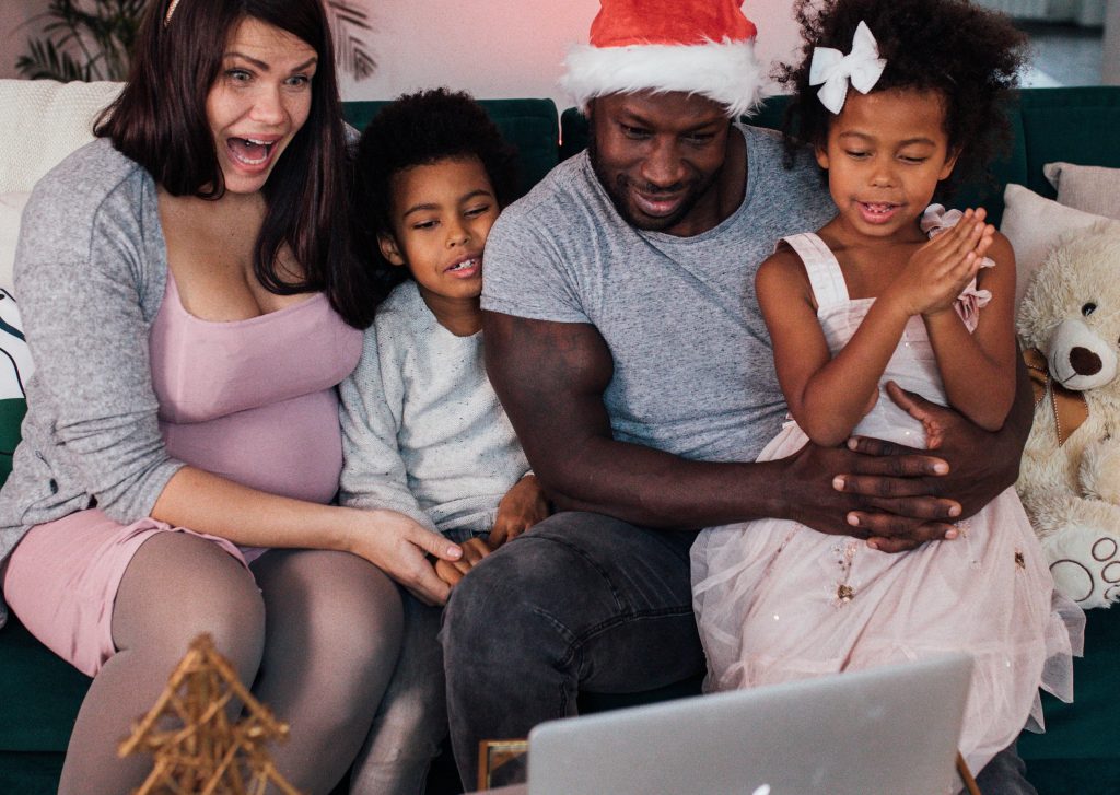 A father, mother and two children in Santa hats smile and point to a computer
