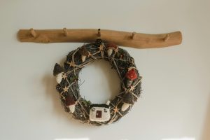 A natural wood wall hook hanger with a Christmas wreath attached to the bottom