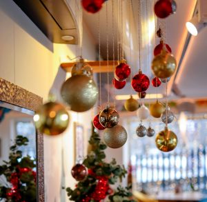 gold and red Christmas ornaments hang from the ceiling with Christmas tree in background