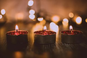 Three lit cranberry-colored tealight candles on a wooden table top
